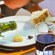 Olive oil pouring out of a bottle onto a piece of cheese next to some bread and a glass of wine